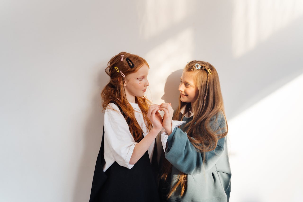 Adorable portrait of two young girls making a heart shape with hands, expressing friendship and joy.