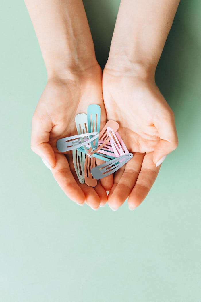 Close-up of hands holding pastel colored hair clips on a mint green background.
